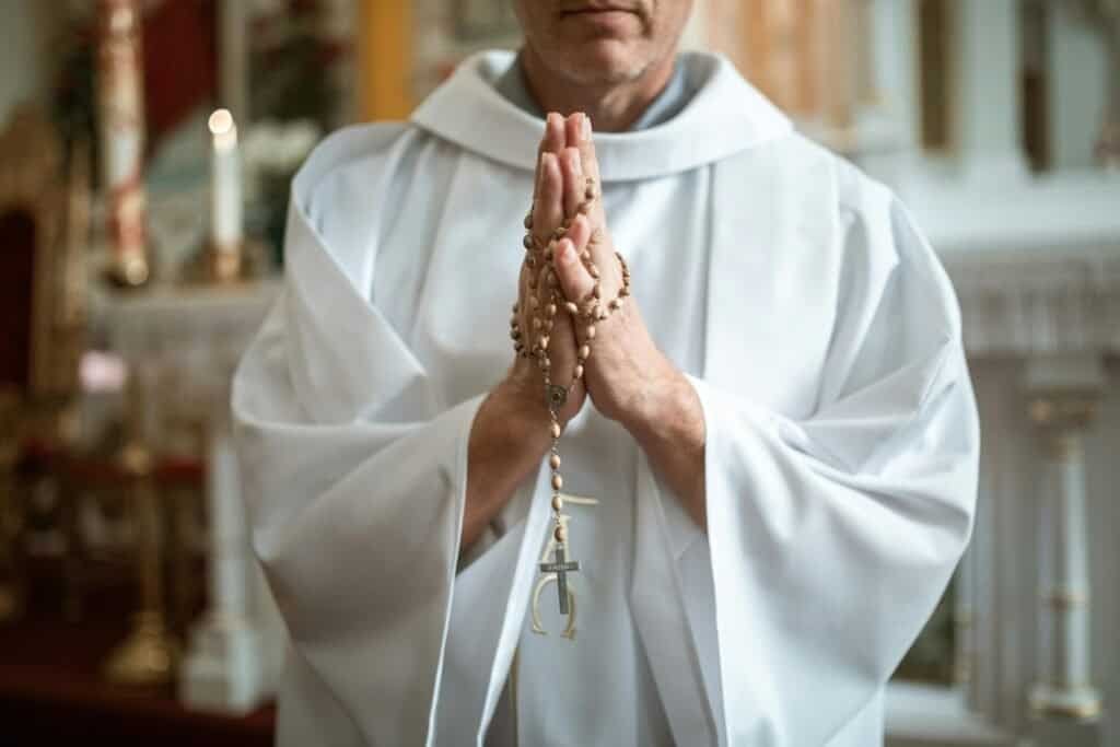 Priest praying in a church with a rosary in his hands