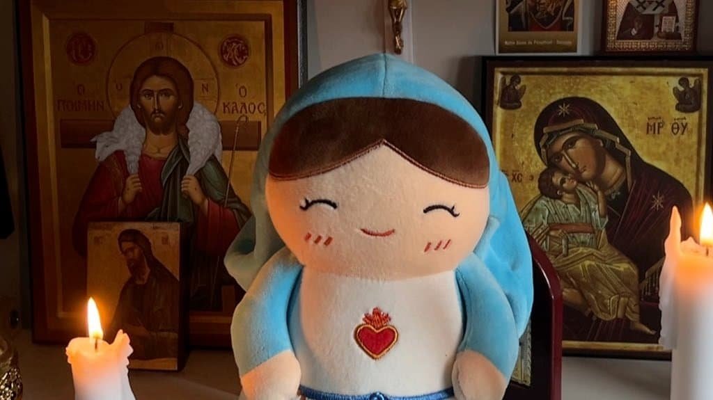 Virgin Mary plushie between two lit candles on a home altar surrounded by icons